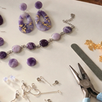 "Diddit Amethyst jewellery components laid out on a light surface, including teardrop drop earrings, a bracelet, round beads, findings, and metal tools including pliers and a nail file."