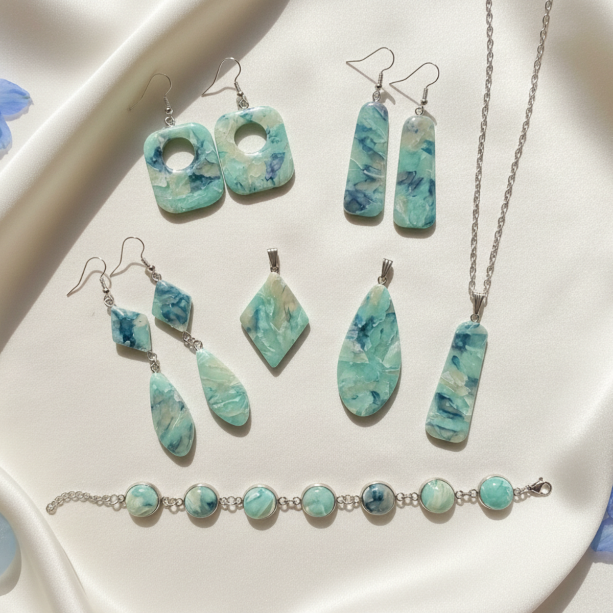 "A Diddit Aquamarine jewellery making experience kit set featuring turquoise and white marbled stone pieces on silver-tone chains, including earrings, a necklace, a pendant, a bracelet, and a matching charm piece, arranged on a white satin surface."