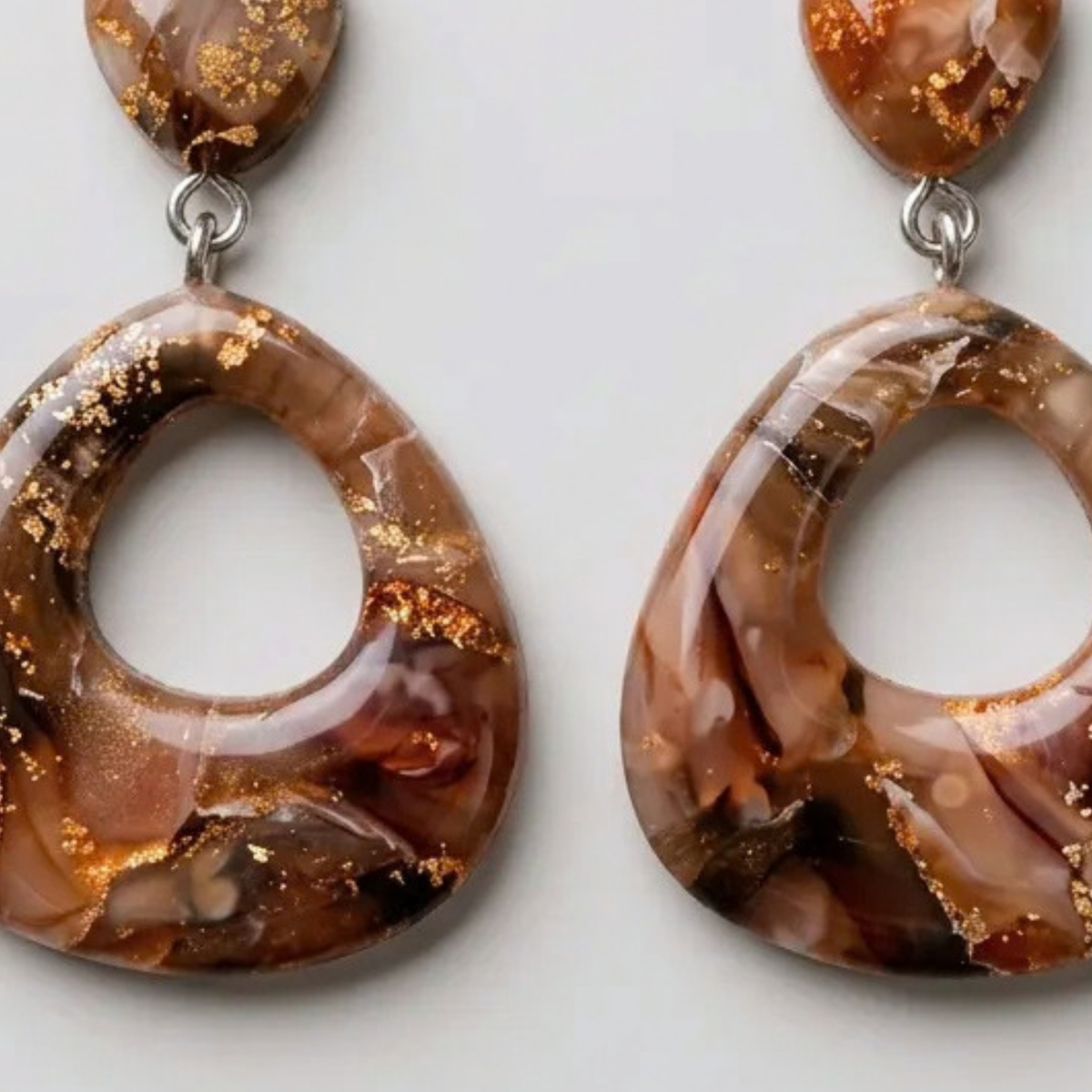 "A pair of Diddit Desert Onyx teardrop drop earrings with a glossy brown and amber marbled finish, accented with shimmering gold foil flakes and silver-tone fishhook wires."