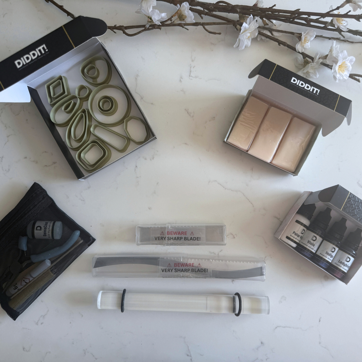 An overhead flat-lay of a Diddit Jewellery Making Experience kit on a white marble surface, featuring various tools, packaging boxes, and accessories.
