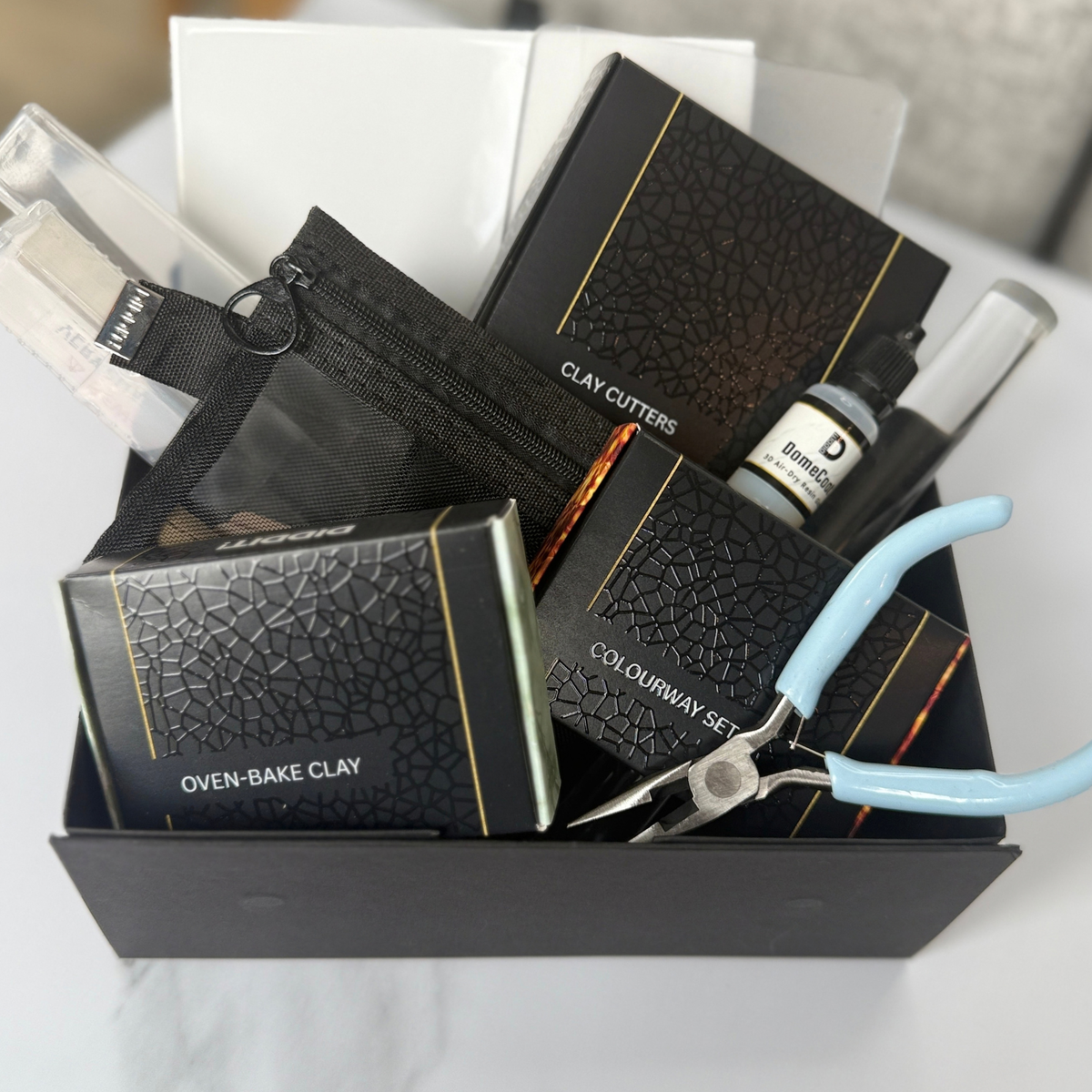 "Diddit Tortoiseshell clay crafting kit tools and materials in a tray, including oven-bake clay, cutters, pigment and blue-handled pliers."