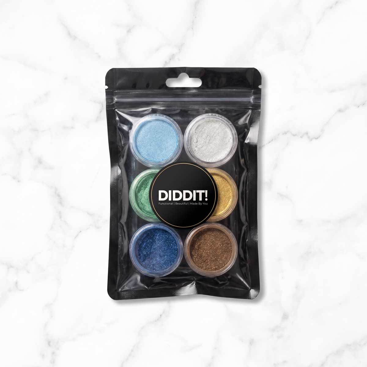A package of six DIDDIT! glitter powders in various colors, sealed in a clear stand-up pouch with a black header, set against a white marble background.