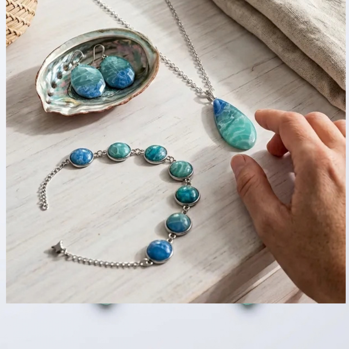 "A Diddit Ocean Effect jewellery set featuring a silver necklace and bracelet with blue and green marbled stone beads, displayed on a light wood surface alongside a hand holding the necklace pendant."